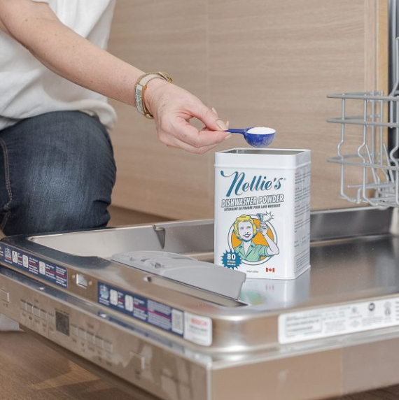 A lady holding a scoop of Nellie's Dishwasher Powder over it's Tin