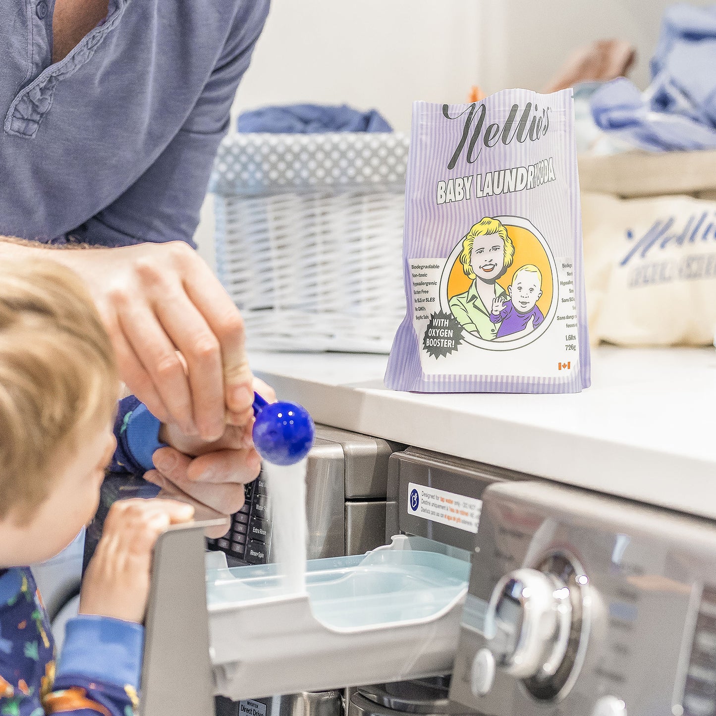 A father holding his son's hand while together pouring a scoop of Baby Laundry Soda into the Washing Machine Detergent Drawer