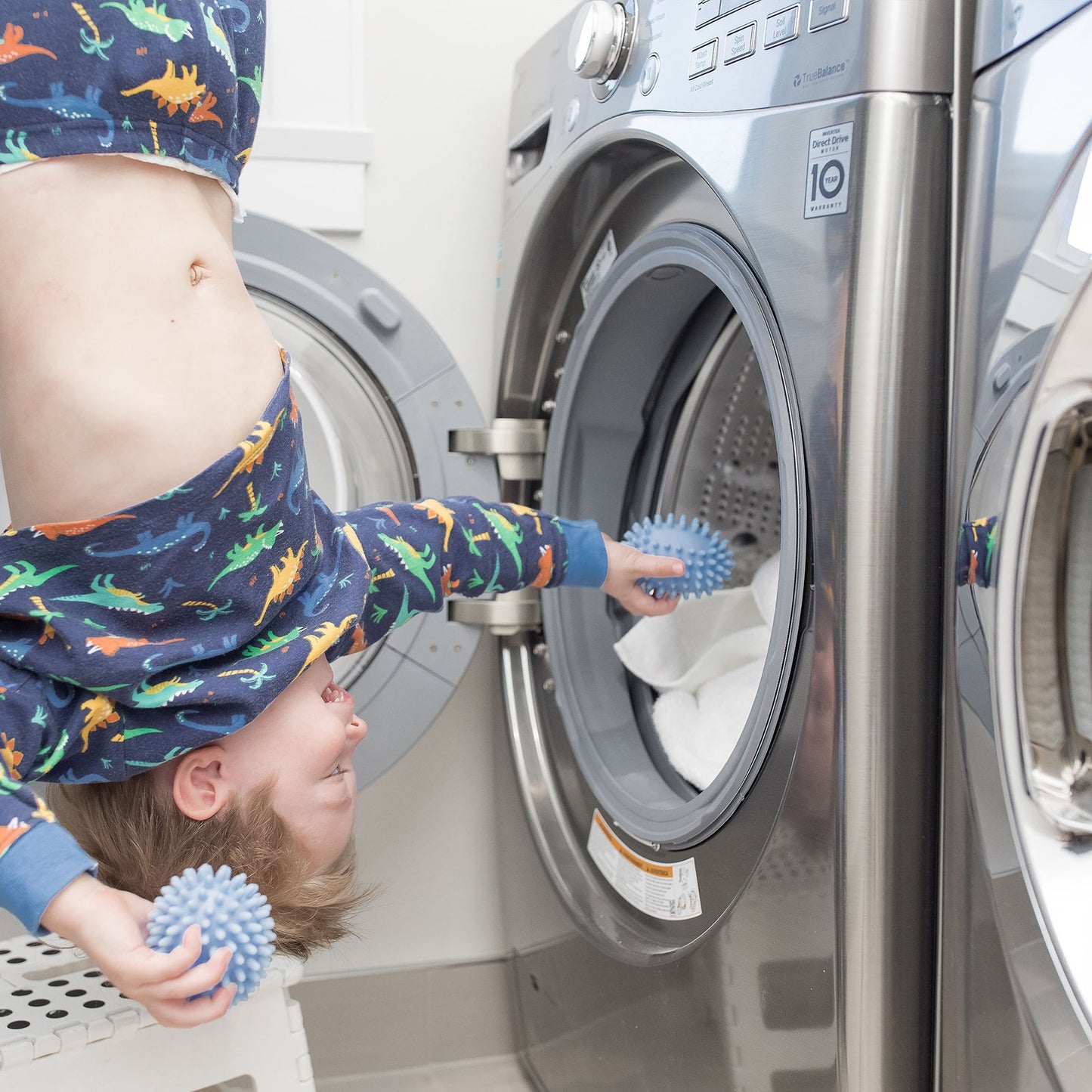A upside down kid holding a dryerball in a hand and putting another dryer ball into the front load washing machine